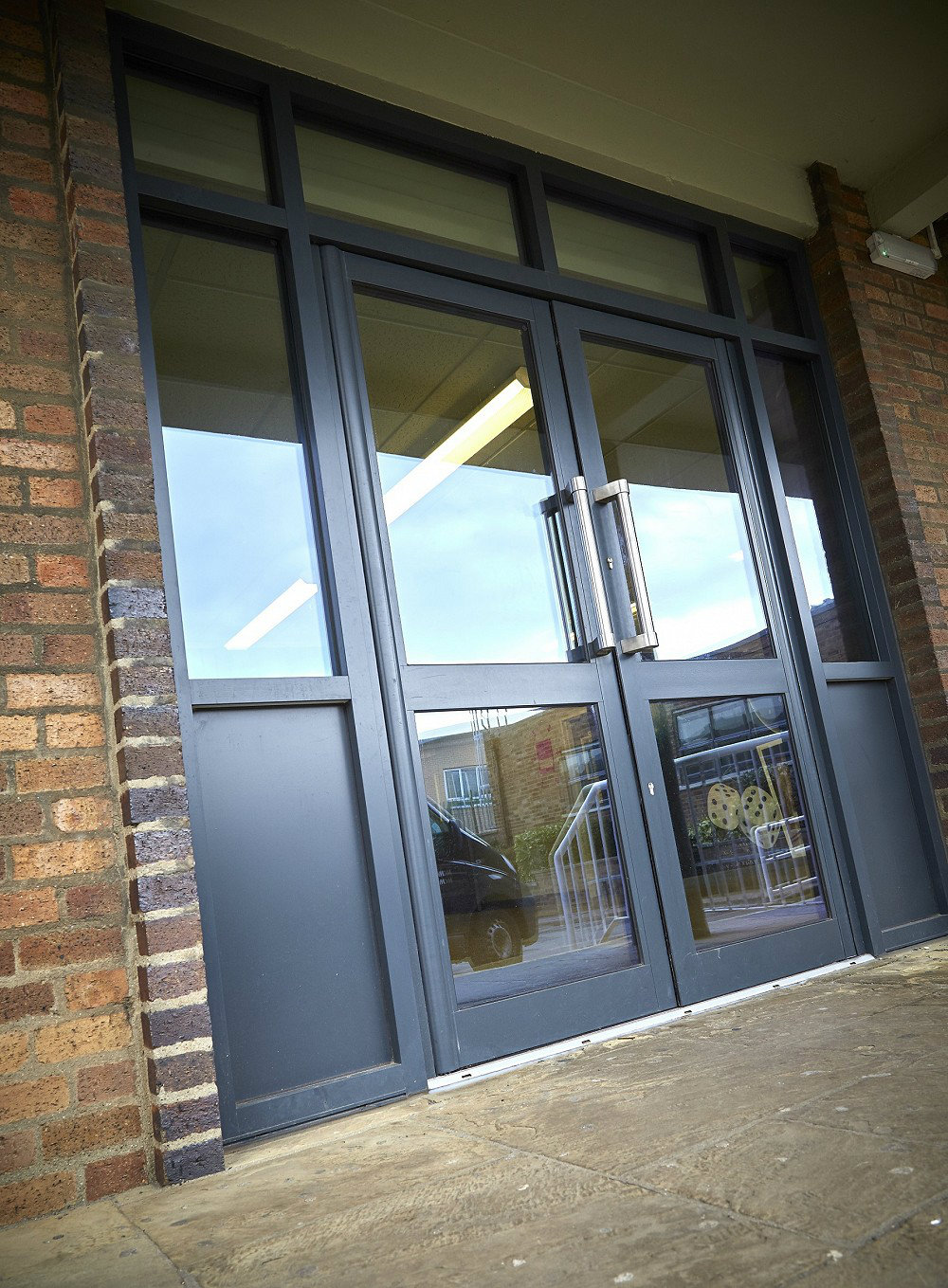 The entrance to a refurbished school which is glazed with grey aluminium doors